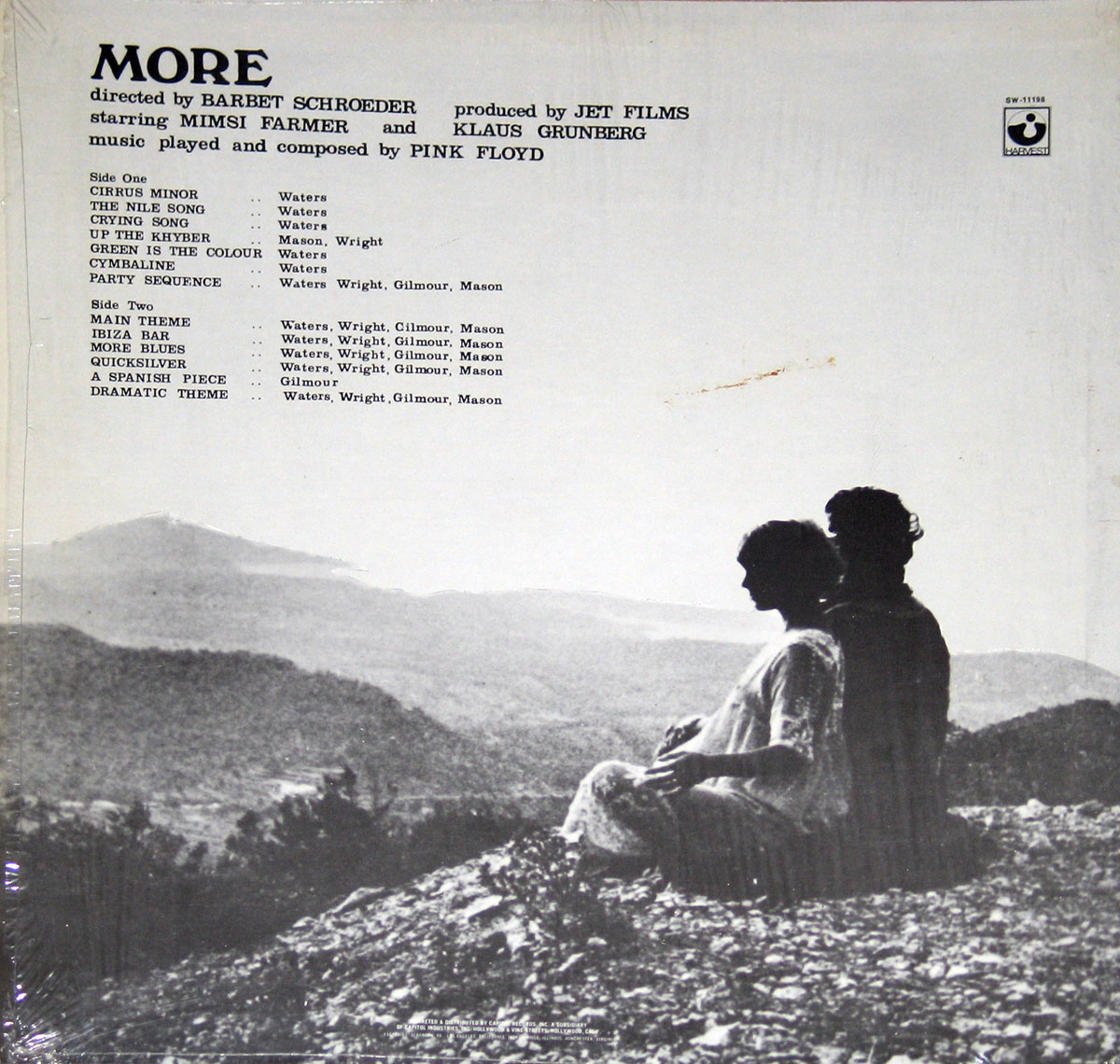 ‘Back cover of Pink Floyd’s More original motion picture soundtrack. The black-and-white image features two silhouetted figures, a man and a woman, sitting on a rocky hilltop overlooking a vast, mountainous landscape, likely in Ibiza. The top section lists the album’s details, including the director Barbet Schroeder, producers Jet Films, starring Mimsi Farmer and Klaus Grünberg, and the tracklist with songwriting credits. A Tower Records logo appears in the top-right corner.’
